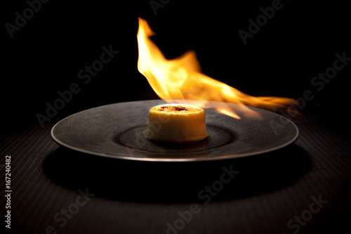 Flamed creme brulee served on plate against black background