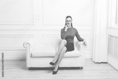 Beautiful woman in red shirt and eyeglasses sitting on a sofa  Monochrome image