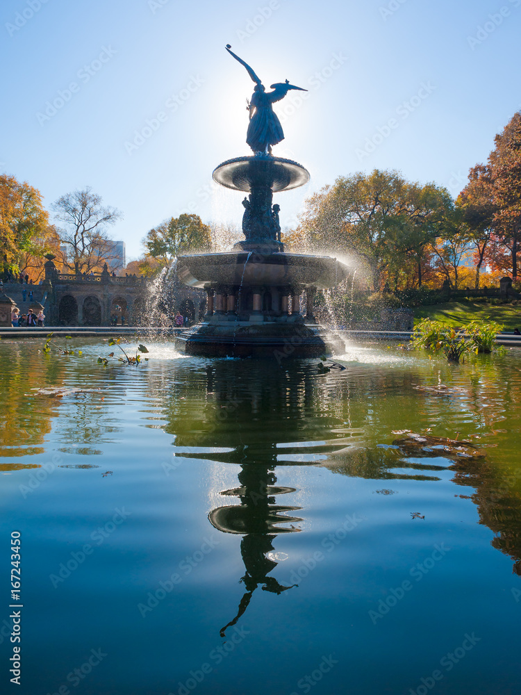 Bethesda Fountain against sun with angel statue reflecting in the water, Central Park, New York, USA