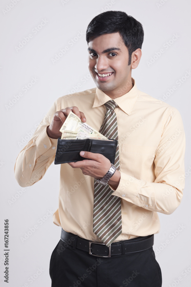 Portrait of happy businessman showing money in wallet against gray background Portrait of happy businessman showing money in wallet against gray background