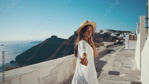 Young sexy woman is on the greek island Santorini in a white dress and and straw hat white greek houses volcano sea sunny weather