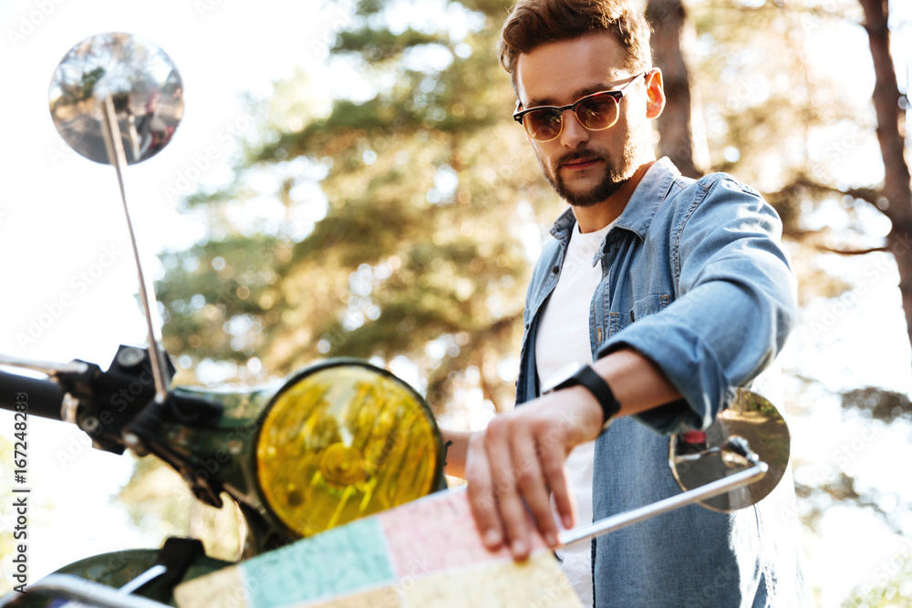 Attractive young bearded man near scooter looking at map