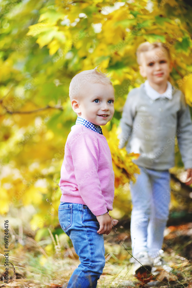 Cheerful little brother and sister standing in the park in autumn Cheerful little brother and sister standing in the park in autumn