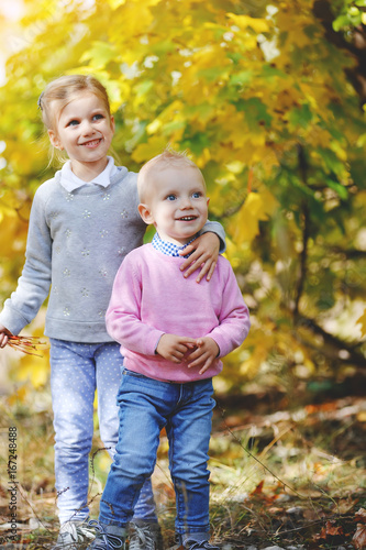 Cheerful little brother and sister standing in the park in autumn