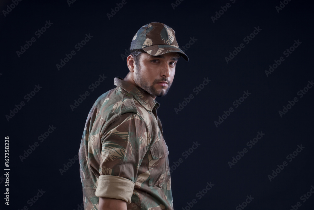 Portrait of young soldier standing over black background 
