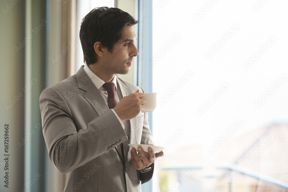 Smart young businessman having cup of tea while thinking Smart young businessman having cup of tea while thinking