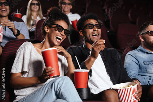 Happy friends sitting in cinema watch film eating popcorn photo