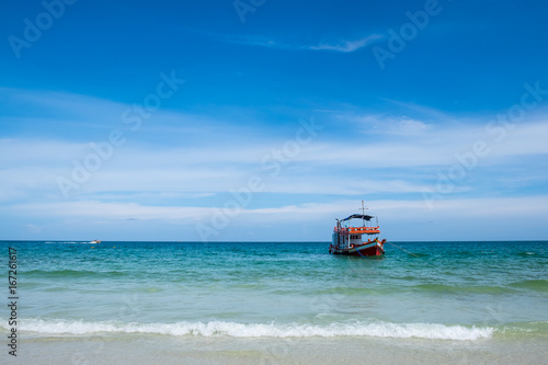 fishing boat on wave of green ocean on sandy beach and blue sky
