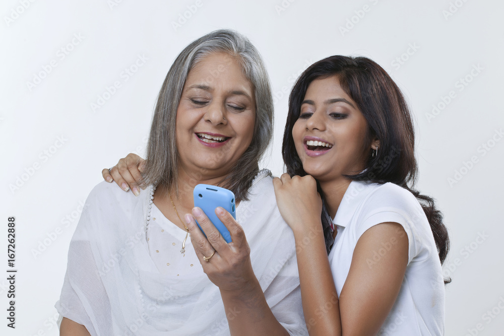 Close-up of a mature woman and her granddaughter looking at a mobile phone and laughing Close-up of a mature woman and her granddaughter looking at a mobile phone and laughing