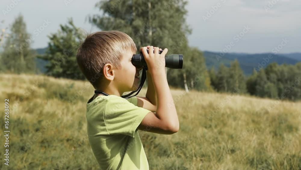 The boy stands on the top of the mountain and looks at the binoculars The boy stands on the top of the mountain and looks at the binoculars