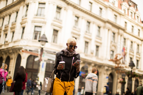 Young black woman with coffee cup and mobile phone on the street