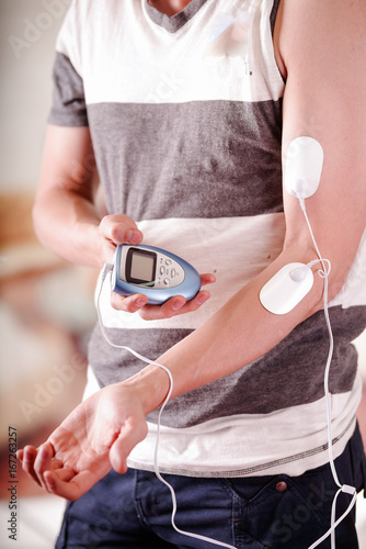 Close-up of a man holding an electrode machine in his hand and with electrostimulator electrodes in the arm of a fitness young man in a blurred background