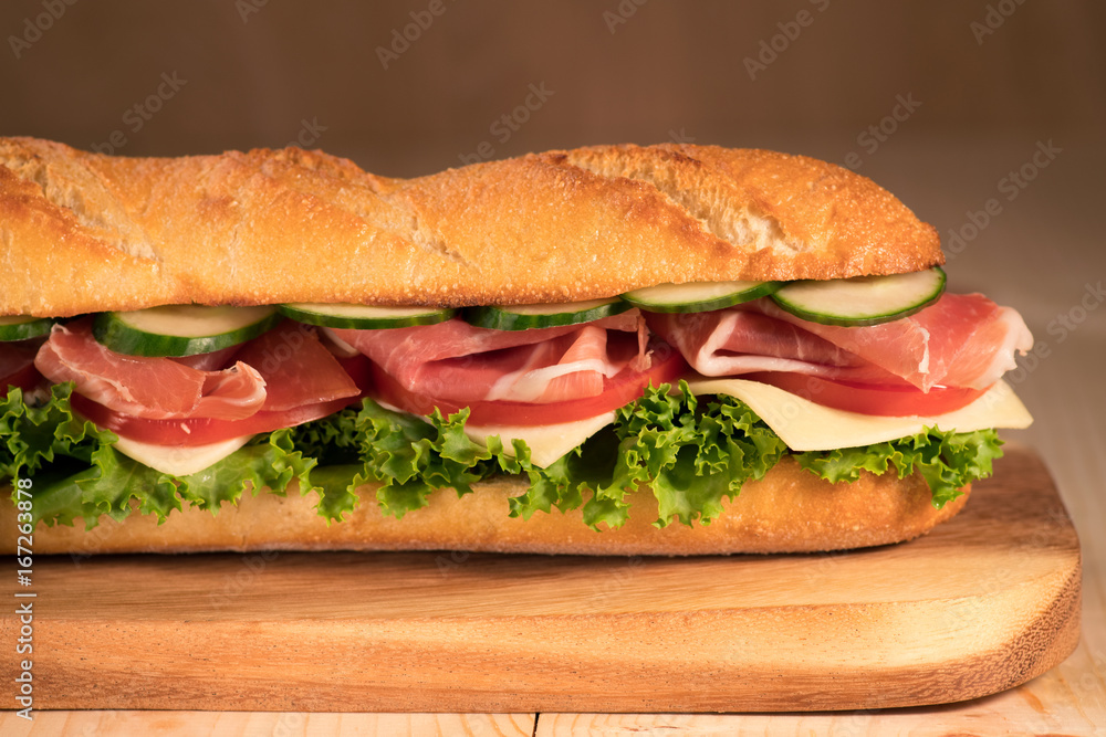 Fresh crispy sandwich with prosciutto, cheese, tomatoes, lettuce, cucumbers on a wooden background.Close Up. Healthy concept. Fresh crispy sandwich with prosciutto, cheese, tomatoes, lettuce, cucumbers on a wooden background.Close Up. Healthy concept.