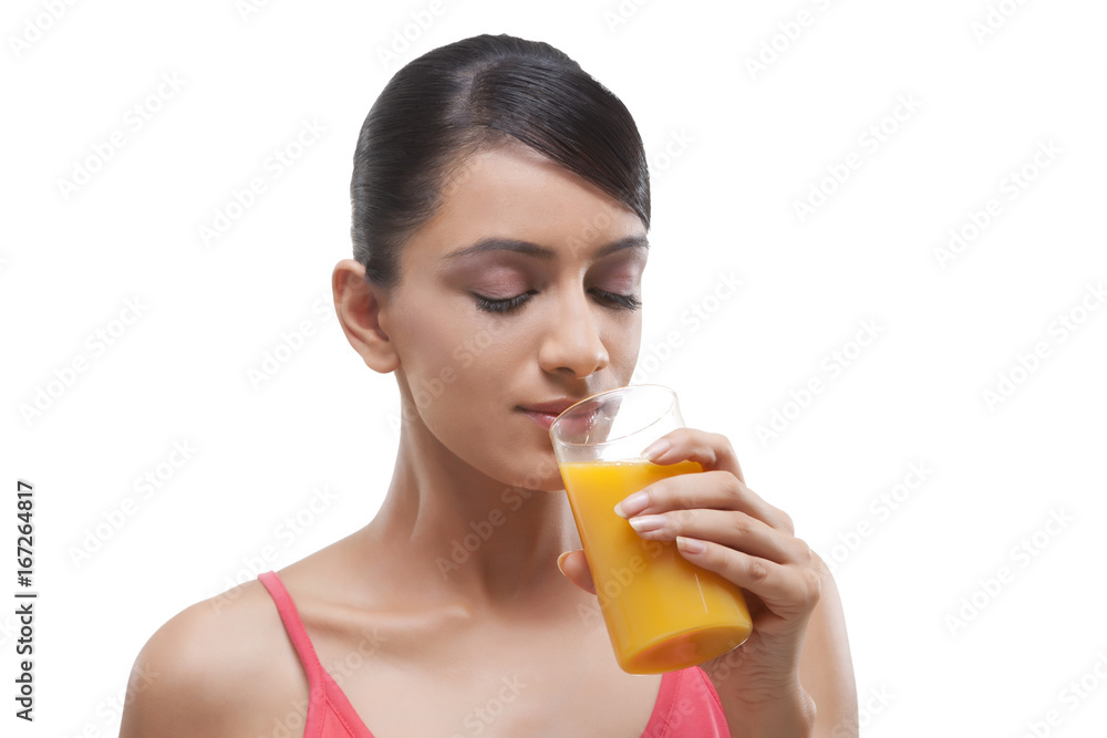 Close-up of beautiful young woman drinking orange juice over white background Close-up of beautiful young woman drinking orange juice over white background