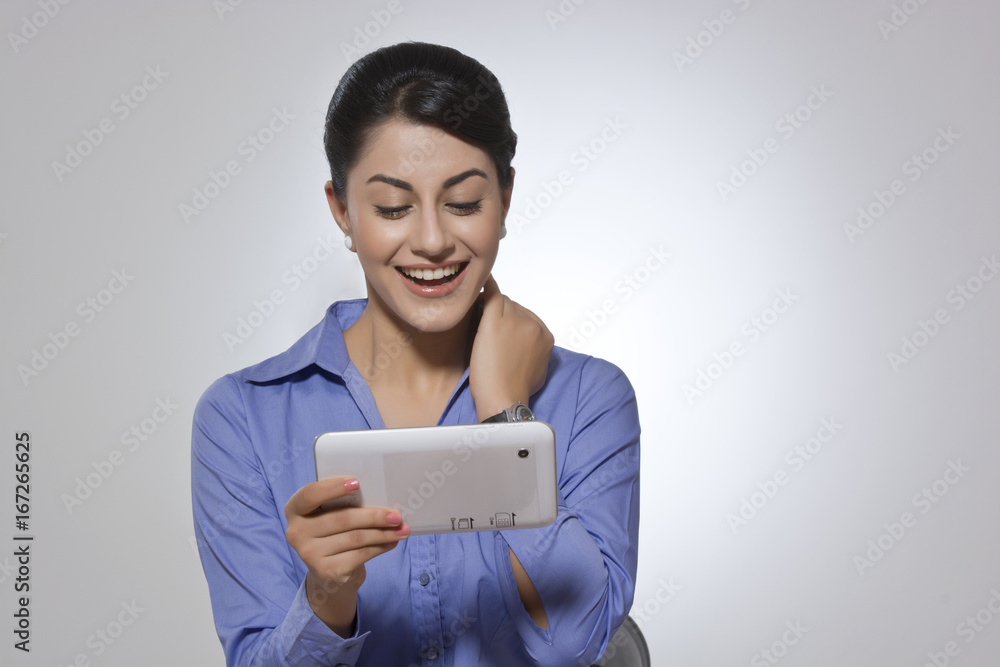 Happy Indian businesswoman using digital tablet against gray background Happy Indian businesswoman using digital tablet against gray background