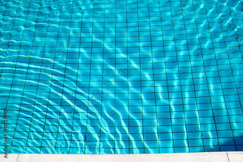 Blue ripped water in swimming pool. Swimming pool bottom caustics ripple and flow with waves background. Clear light blue pool water ripples with sun reflections. Surface of blue swimming pool. © zoranlino
