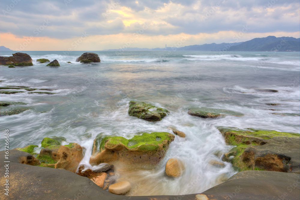 Obraz premium Dramatic dawning sky with golden clouds over the rocky coast ~ Scenery of rising sun illuminating the sea water at a rocky beach ( Long Exposure Effect )