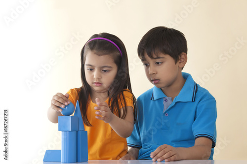 Cute sister and brother stacking geometric shapes against colored background