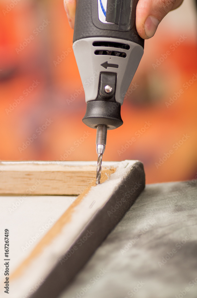 Closeup of a hardworker man drilling a wooden frame with his drill over a gray table in a blurred background