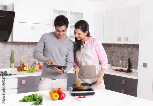 Couple looking at digital tablet and cooking