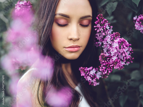 Beautiful young woman surrounded by flowers of lilac