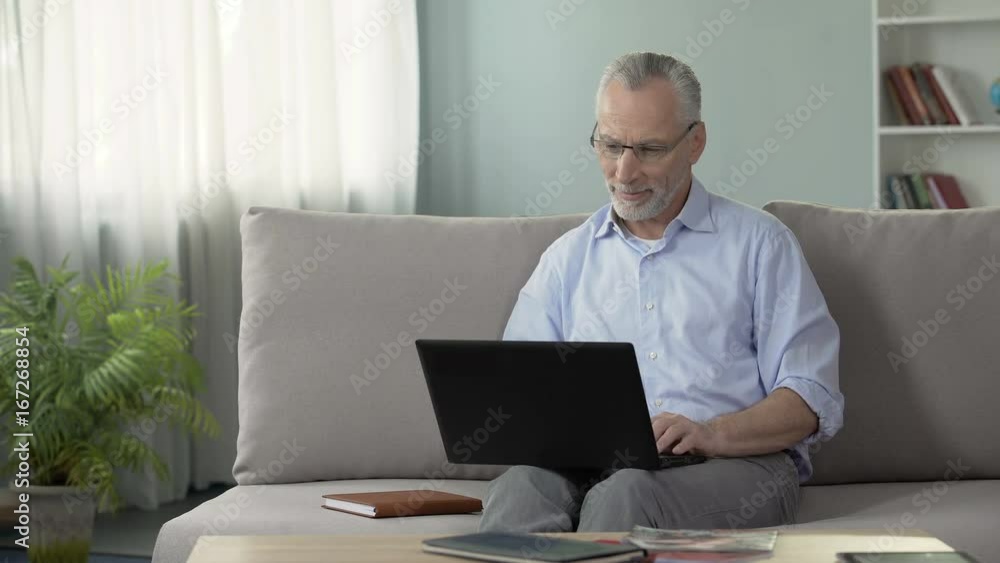 Healthy senior male sitting on sofa and viewing photos on dating website, laptop Healthy senior male sitting on sofa and viewing photos on dating website, laptop
