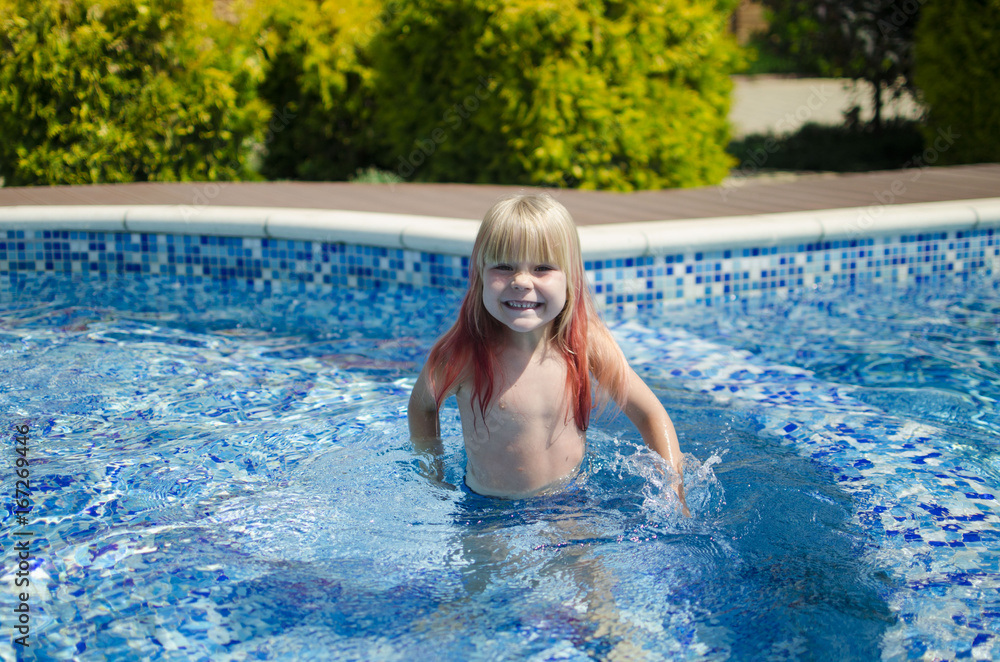 Blond little girl in the swimming pool. Happy smiling girl