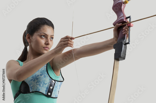 Young woman practicing archery against gray background photo