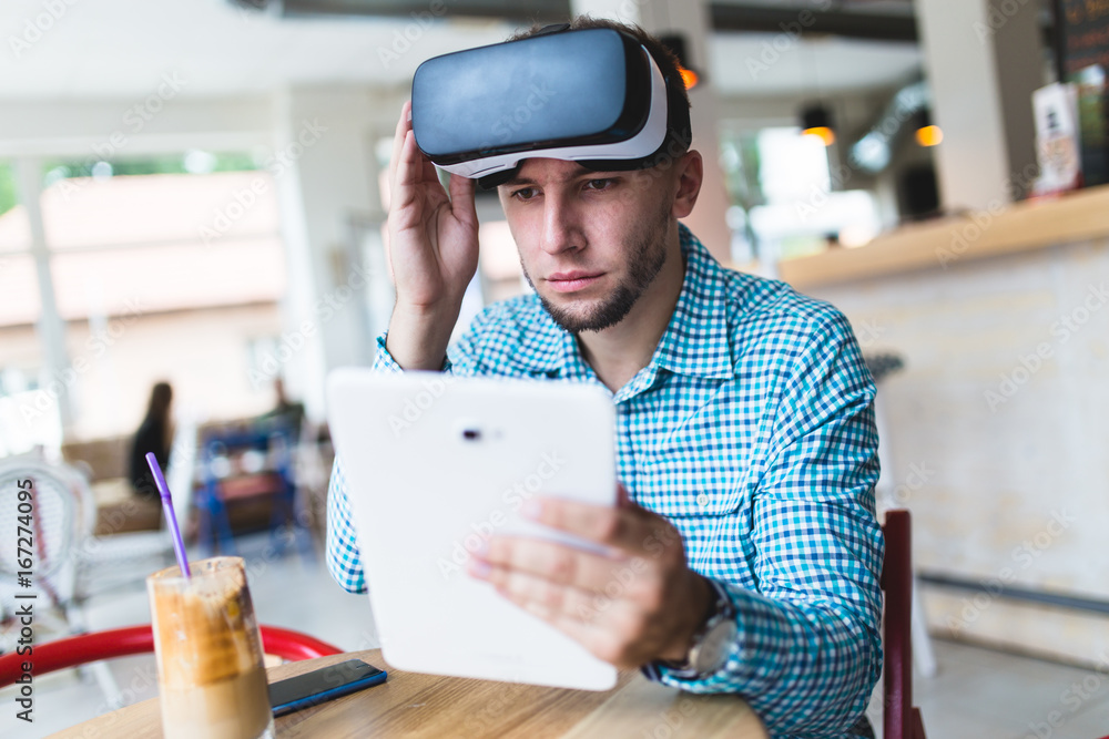 Young handsome man sitting in cyber cafe and using virtual reality headset or glasses. Young handsome man sitting in cyber cafe and using virtual reality headset or glasses.