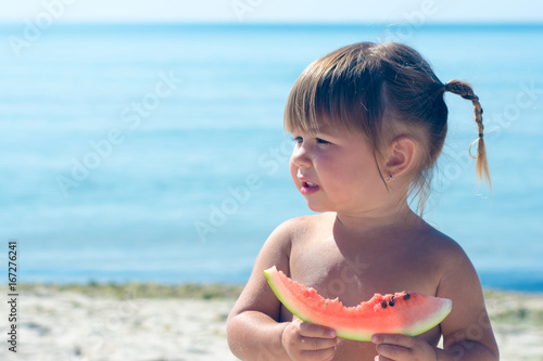 Funny little girl eating watermelon at the beach