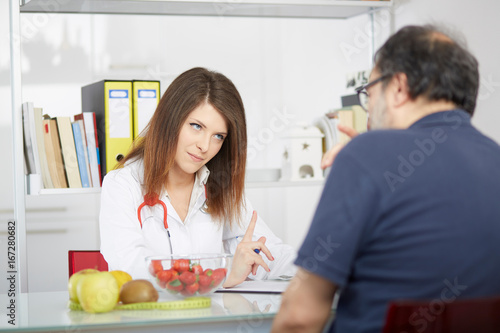 Smiling doctor nutritionist giving fruit to male patient sitting at the desk