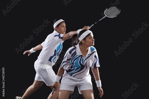 Young female partners in sportswear playing badminton over black background © IndiaPix