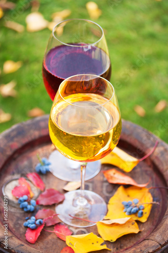 Glasses of red and white wine with grape on old wine barrel outside