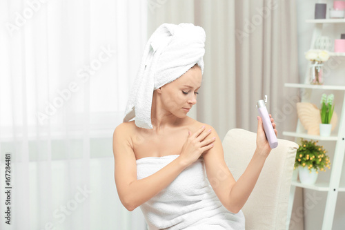 Beautiful young woman after bath applying body cream onto skin at home