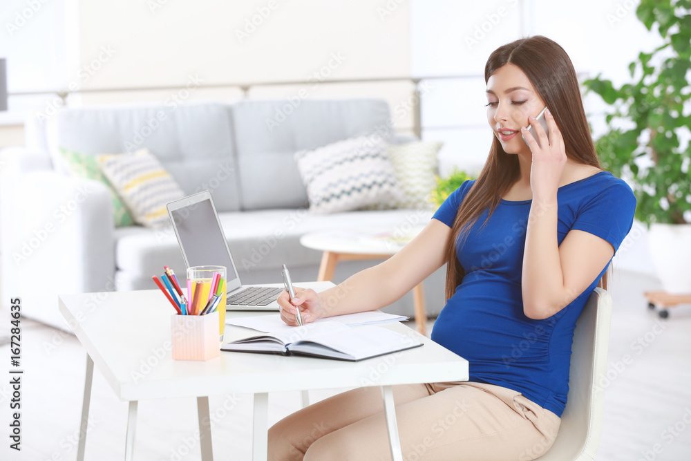 Young beautiful pregnant woman talking by phone while working at home Young beautiful pregnant woman talking by phone while working at home