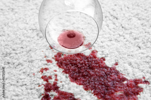 Glass of red wine spilled on white carpet, close up