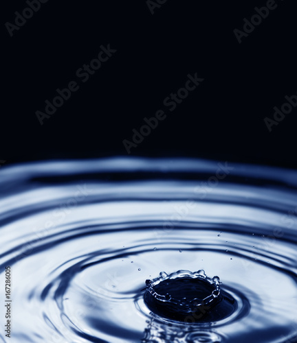 Beautiful water droplet splashing. Rings waves on black blue background. soft focus copy space.