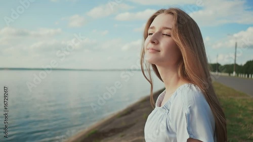 Cute young girl sitting on the seashore watching the setting sun and posing smiling. photo