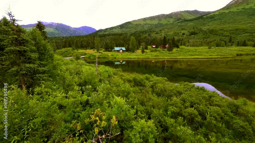 Alaska Sterling Highway 4k Drone tracking shot over bushes then over glassy calm lake to rustic old mountain cabins with mountains in the background. Alaska Sterling Highway 4k Drone tracking shot over bushes then over glassy calm lake to rustic old mountain cabins with mountains in the background.