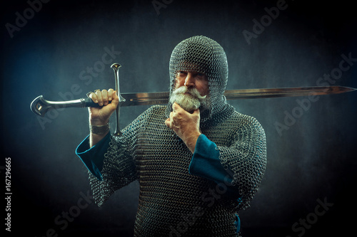Powerful bearded knight with the sword on the dark background
