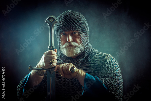 Powerful bearded knight with the sword on the dark background