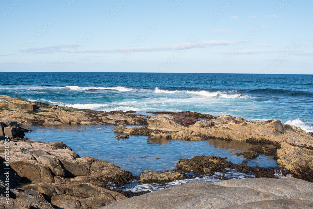 Blue sky, ocean and rock formations - coastline and rockpool on a sunny winter's day at Bingi, near Moruya in NSW, Australia