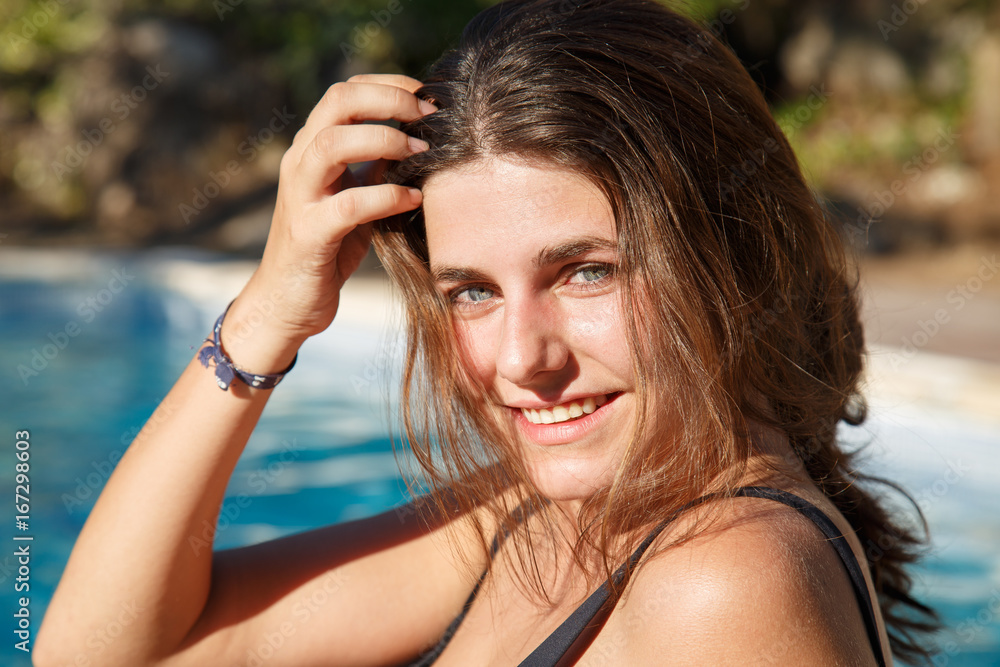 Portrait of young brunette smiling happily at camera while posing on background of pool.  