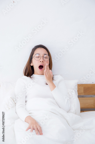 Beautiful asian woman waking up and yawn in bed in the bedroom, healthcare concept.