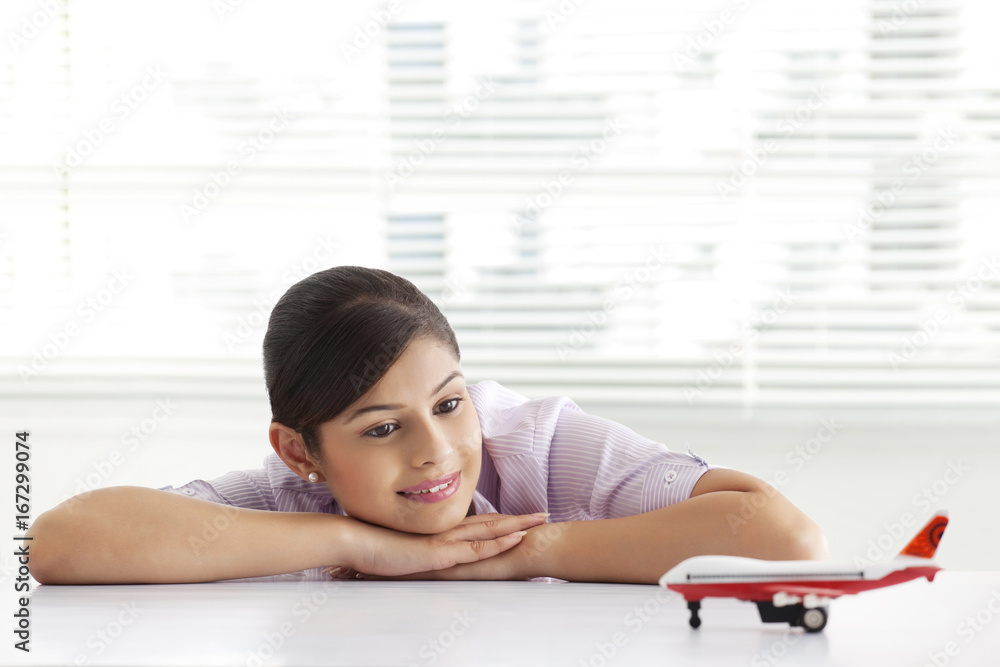 Thoughtful young business woman looking at airplane model Thoughtful young business woman looking at airplane model