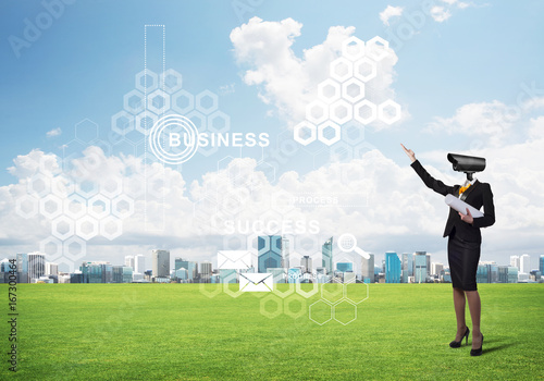 Camera headed woman standing on green grass against modern cityscape