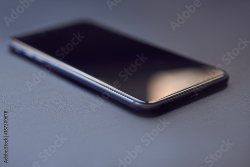 Closeup of a phone lying on a black table. On the screen there are glare from the window