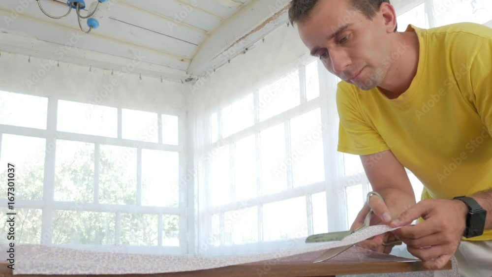 A designer clothes designer notes and cuts fabric details with scissors. Very bright room with windows. The concept of designing. A designer clothes designer notes and cuts fabric details with scissors. Very bright room with windows. The concept of designing.