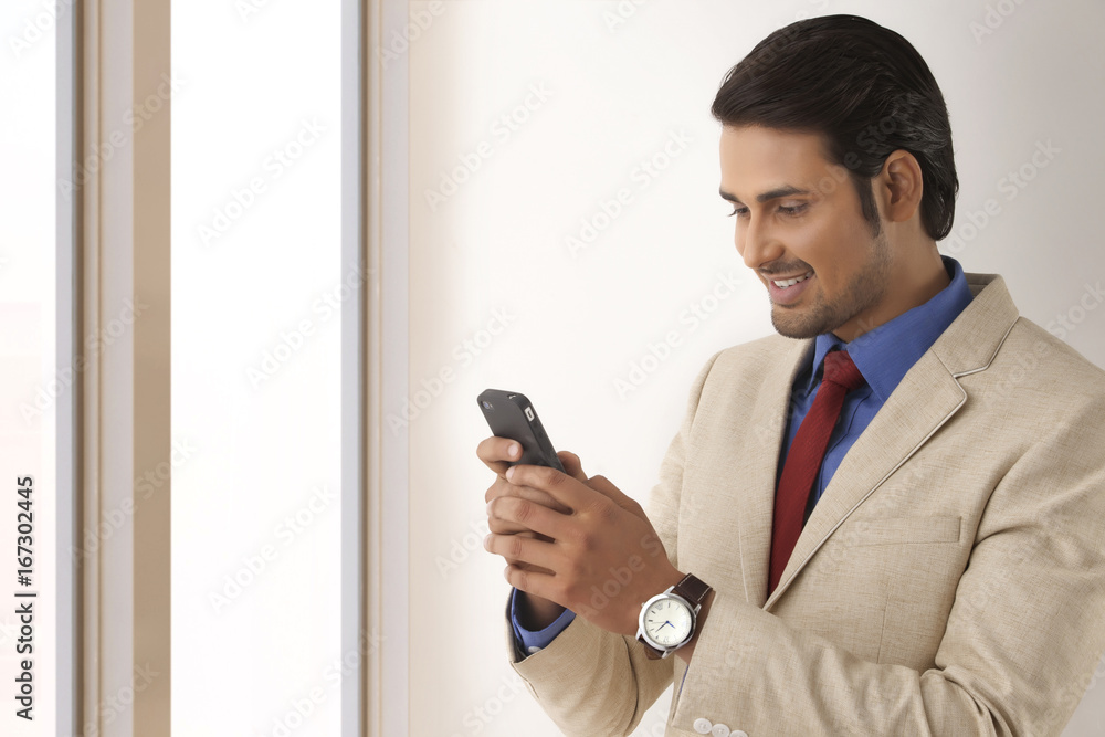 Young Indian businessman reading text message through smart phone in office Young Indian businessman reading text message through smart phone in office