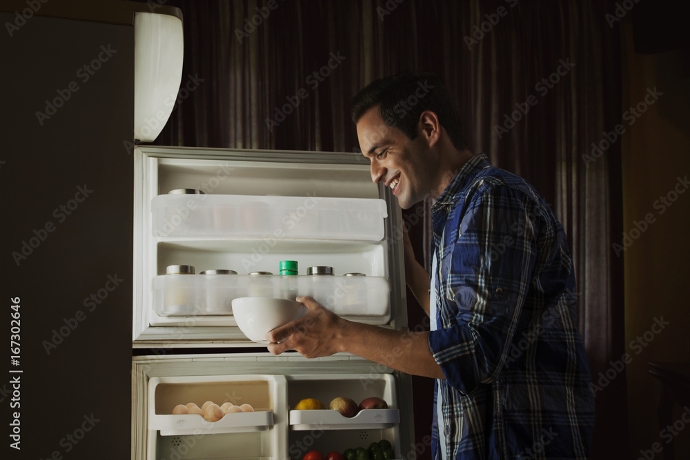 Young man standing in the kitchen searching food in the fridge at night Young man standing in the kitchen searching food in the fridge at night